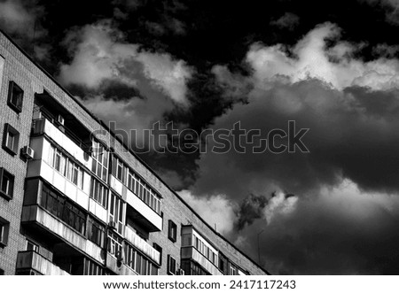 The last floors of a brick multi-story building against the background of a blue sky with white clouds. City sketches, stone jungle. Black and white photo
