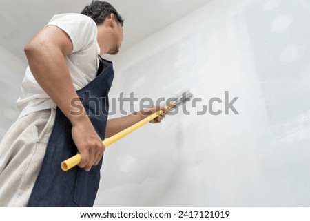 painter man, brush in hand for products to restore and paint the wall, indoor the building site of a house, wall during painting, renovation, painting, contractor, Architect, construction worker Royalty-Free Stock Photo #2417121019