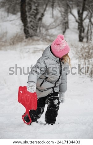 A girl in a snowy forest rides an ice slide down a slide. Photo of a child in a winter forest. Winter, winter holidays, vacations, vacations.