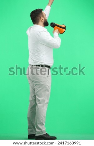A man, full-length, on a green background, with a megaphone