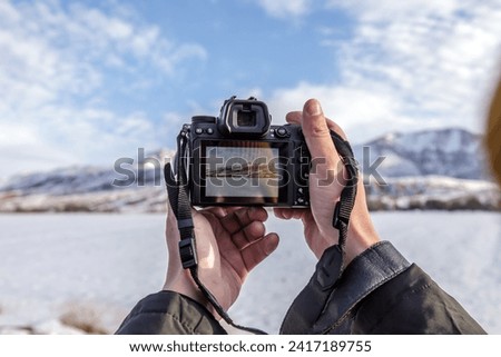 A photographer is photographing the landscape. He is holding the camera. There is a picture of the landscape on the camera's display.