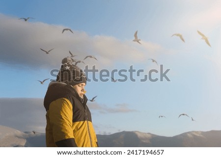 A girl basks in the sun on a winter walking day on the seashore against the backdrop of mountains.