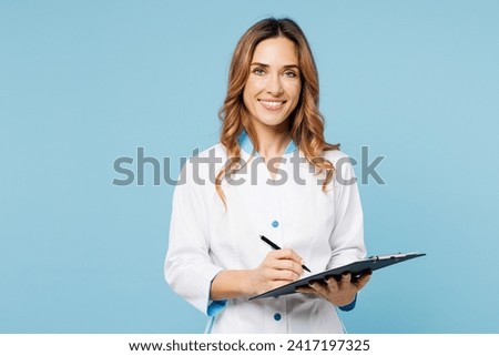 Female cheerful happy doctor woman she wearing white gown suit work in hospital clinic office holding clipboard sign medical documents isolated on plain blue background. Health care medicine concept