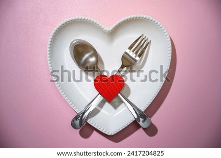 Heart plate with silverware of fork and knife with a red heart over a pink background. Romantic dinner Valentine's Day concept