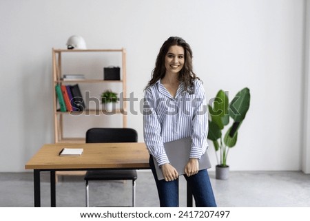 Smiling businesswoman holding open laptop in office Royalty-Free Stock Photo #2417207497