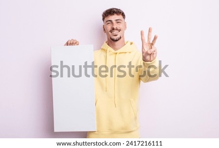 young handsome man smiling and looking friendly, showing number three. blank canvas concept