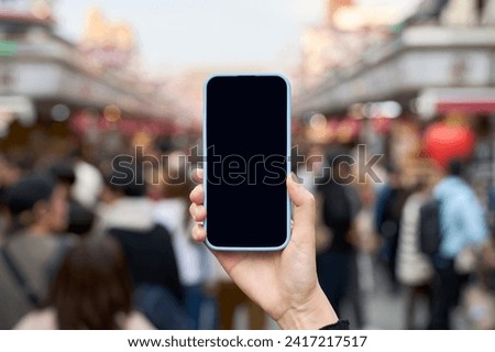 Crowded tourist spot in Japan and a hand holding a smartphone                  