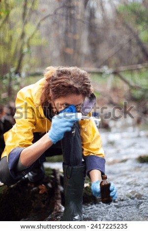 Concentrated Caucasian Female Environmental Biologist Collecting Samples of Water for Further Examination from a Water Stream
