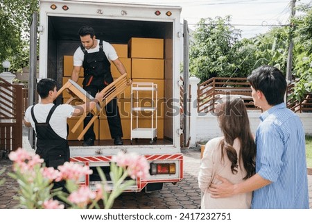 Moving house made easy for a couple with the help of a professional delivery team. They work together unloading and lifting cardboard boxes for efficient relocation. Moving Day Concept Royalty-Free Stock Photo #2417232751