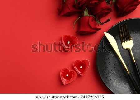 Place setting with heart shaped candles and bouquet of roses for romantic dinner on red table, flat lay. Space for text Royalty-Free Stock Photo #2417236235