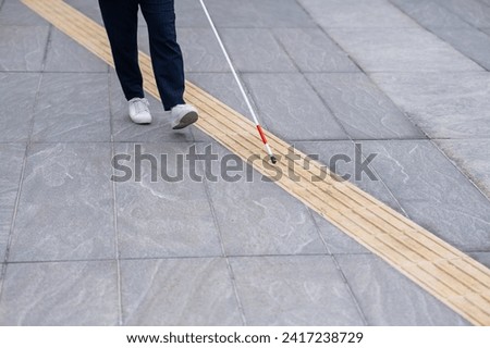 Close-up of the legs of a blind businesswoman walking along a tactile tile with a cane. 