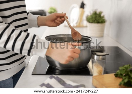Woman with wooden spoon cooking soup in kitchen, closeup Royalty-Free Stock Photo #2417249227