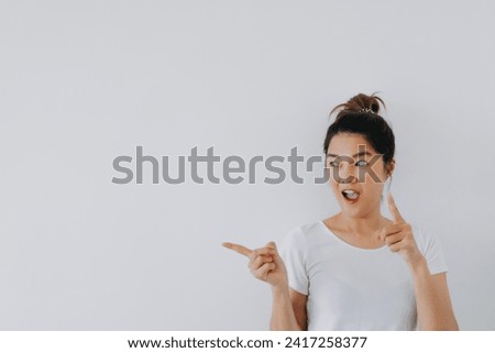Asian Thai woman wow surprised face and pointing fingers to empty space, recommending something at blank background, standing isolated over white wall. High quality photo
