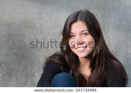 Outdoor portrait of a happy teenage girl smiling in front of a gray wall