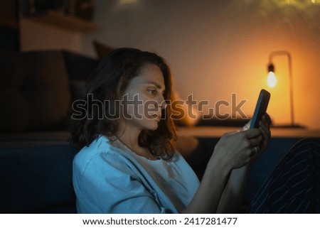 Young woman looking at smartphone screen while sitting at home in the evening