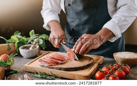 a chefs hands close up on a cozy italian restaurant cutting prosciutto Royalty-Free Stock Photo #2417281877