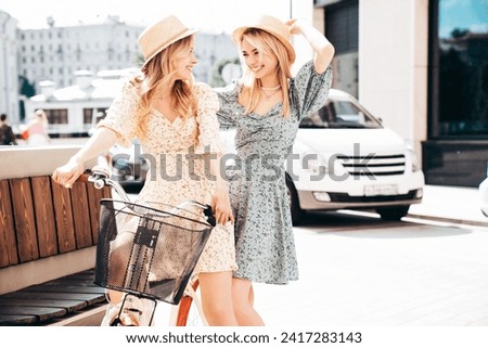 Two young beautiful smiling hipster woman in trendy summer sundress. Carefree women riding retro bicycle. Positive models having fun on bike posing in the park in hats. Best friends outdoors Royalty-Free Stock Photo #2417283143