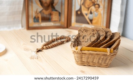 Bread in a wicker basket, rosaries and icons on a wooden table during the great Christian Lent, Lenten food during the Great Orthodox Lent. Royalty-Free Stock Photo #2417290459