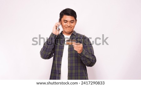 Asian man smiling when in a call and holding credit card over gray background