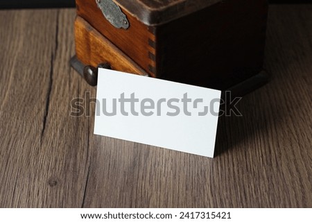 Blank business card mockup with vintage coffee grinder on wooden table background. Mock up for branding identity. Empty template for your design.