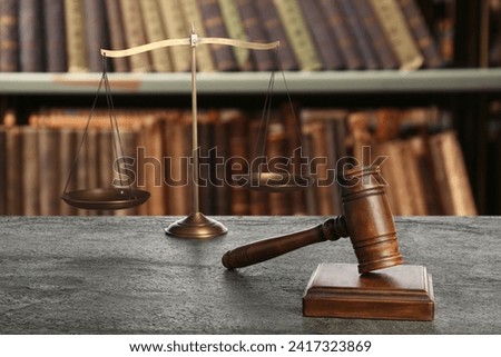 Law. Judge's gavel and scale of justice on grey table against shelves with books indoors