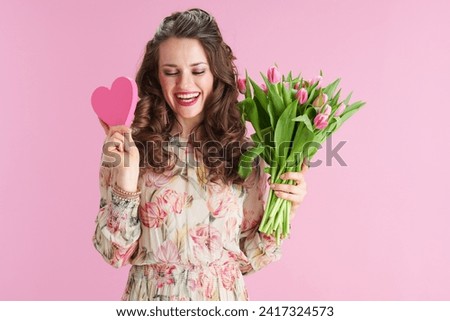 happy trendy female in floral dress with tulips bouquet and pink heart isolated on pink. Royalty-Free Stock Photo #2417324573