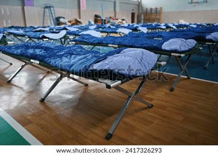 Cots with sleeping bags are placed in the school gym during an emergency Royalty-Free Stock Photo #2417326293