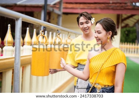 Candid picture angle of couple wearing traditional Thai clothing joins together to make merit at a temple in Thailand.