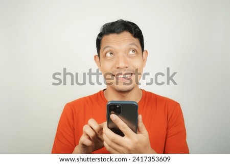 Asian man in orange t-shirt gets idea or idea to solve problem on smartphone on isolated background
