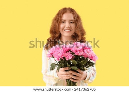 Happy young woman with bouquet of pink chrysanthemum flowers on yellow background. International Women's Day