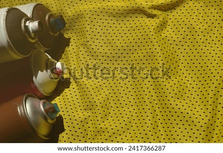 Several used aerosol paint sprayers lie on the sports shirt of a basketball player made of polyester fabric. The concept of youth street art, active sports and eventful lifestyle