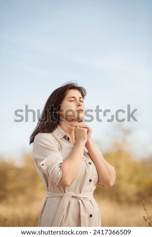 autumn portrait of young woman praying on nature, girl thanks God with her hands folded under chin, concept of religion