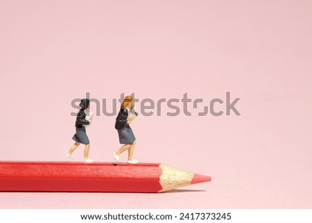 Miniature tiny people toys photography. Two girl students running above red pencil color. Isolated on pink background. Image photo