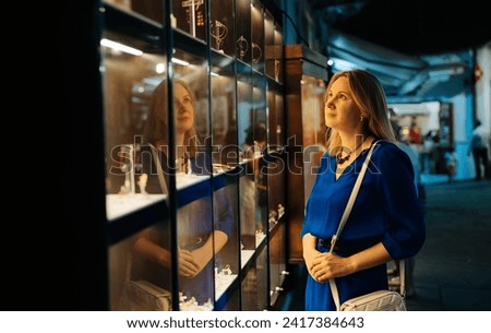 Woman looks at jewelry in store showcase at evening. Royalty-Free Stock Photo #2417384643