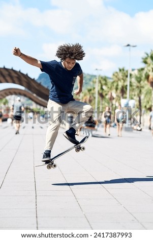 Full length of jumping boy with afro hairstyle performing trick on his skate in sunny city. Barcelona.