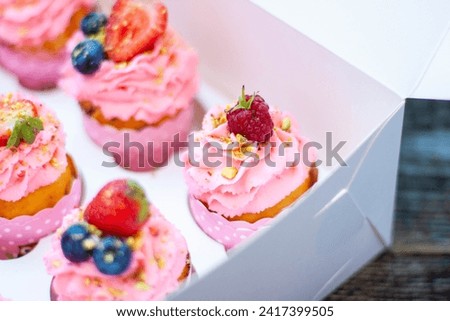 Festive pink cupcakes with fresh strawberries, raspberries and blueberries on cardboard box with chopped pistachios on the top