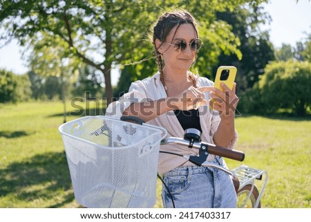 European young woman in park with bicycle and talking on mobile phone. 