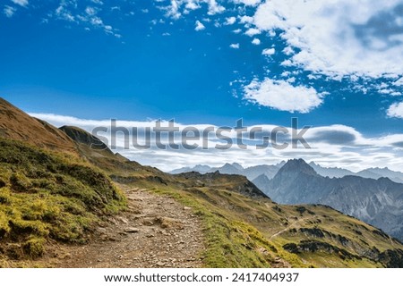 Curved hiking path near Nebelhorn mountain Oberstdorf, Allgäu, with view over distant endless mountain landscape. Shallow depth of field focus on hiking trail Royalty-Free Stock Photo #2417404937