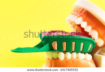 Green dental spoon for taking a dental impression in a mock-up of a dental jaw on a yellow background. Making an artificial jaw for malocclusion. Manufacturing of dental prostheses Royalty-Free Stock Photo #2417405925