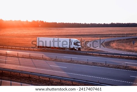 A modern truck with a refrigerator semi-trailer with refrigeration equipment transports flower products while maintaining the temperature regime against the backdrop of sunset and forest.  Royalty-Free Stock Photo #2417407461