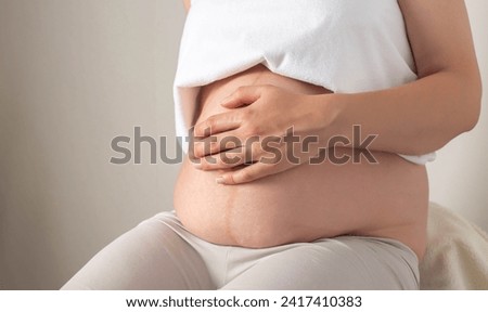 A pregnant girl sits with a bare belly in the office of a cosmetologist and massage therapist. Concept of skin care on the abdomen during pregnancy. Skin changes and stretch marks due to hormonal  Royalty-Free Stock Photo #2417410383