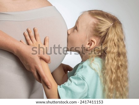 A little girl kisses the belly of her pregnant mother. The concept of motherhood and love for children.