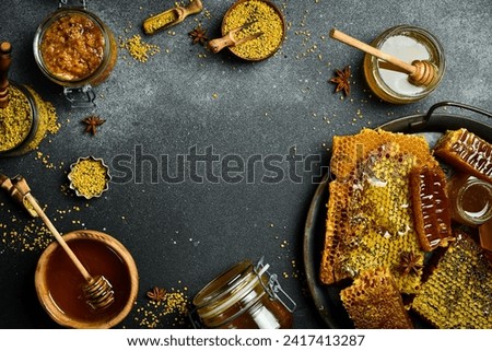 Honey banner. Honeycombs, honey in jars and flower pollen. On a black stone background