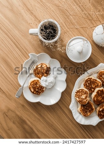 Breakfast served on a wooden table - coffee and pancakes with sour cream, top view    Royalty-Free Stock Photo #2417427597