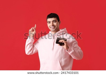 Young male photographer with camera pointing at something on red background
