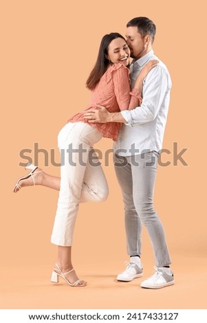 Happy young couple dancing on beige background