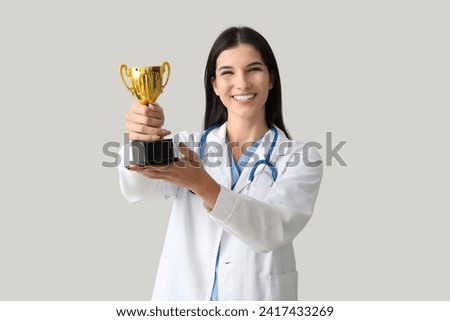 Female doctor with gold cup on light background Royalty-Free Stock Photo #2417433269
