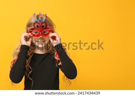 Pretty little girl wearing carnival mask on yellow background Royalty-Free Stock Photo #2417434439