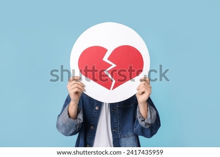 Handsome young man with heart dislike icon on blue background