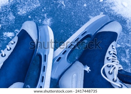 The pair of ice skates on frozen surface of pond or lake. Outdoor winter activity equipment.